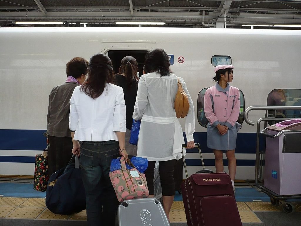 Travelers with rolling suitcases waiting to board a Shinkansen on the platform