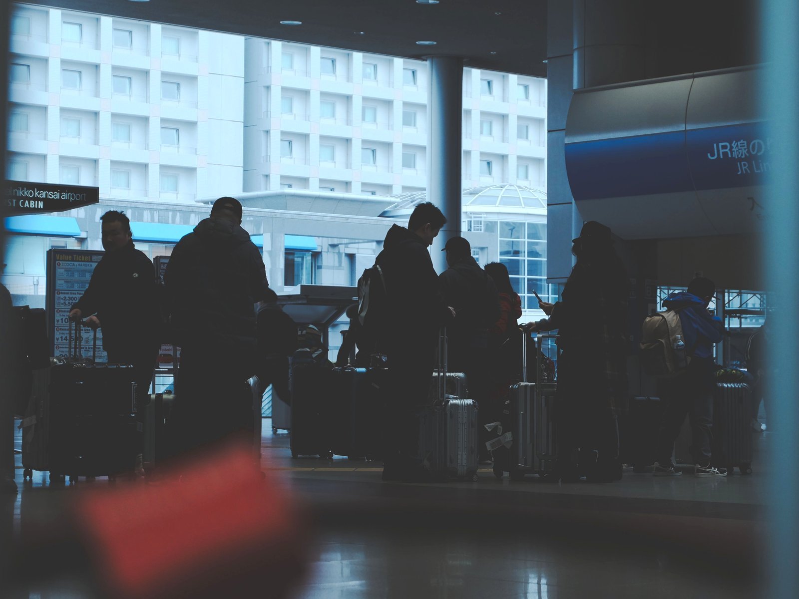Silhouetted travelers with rolling suitcases waiting near the JR line entrance at a Japanese airport station