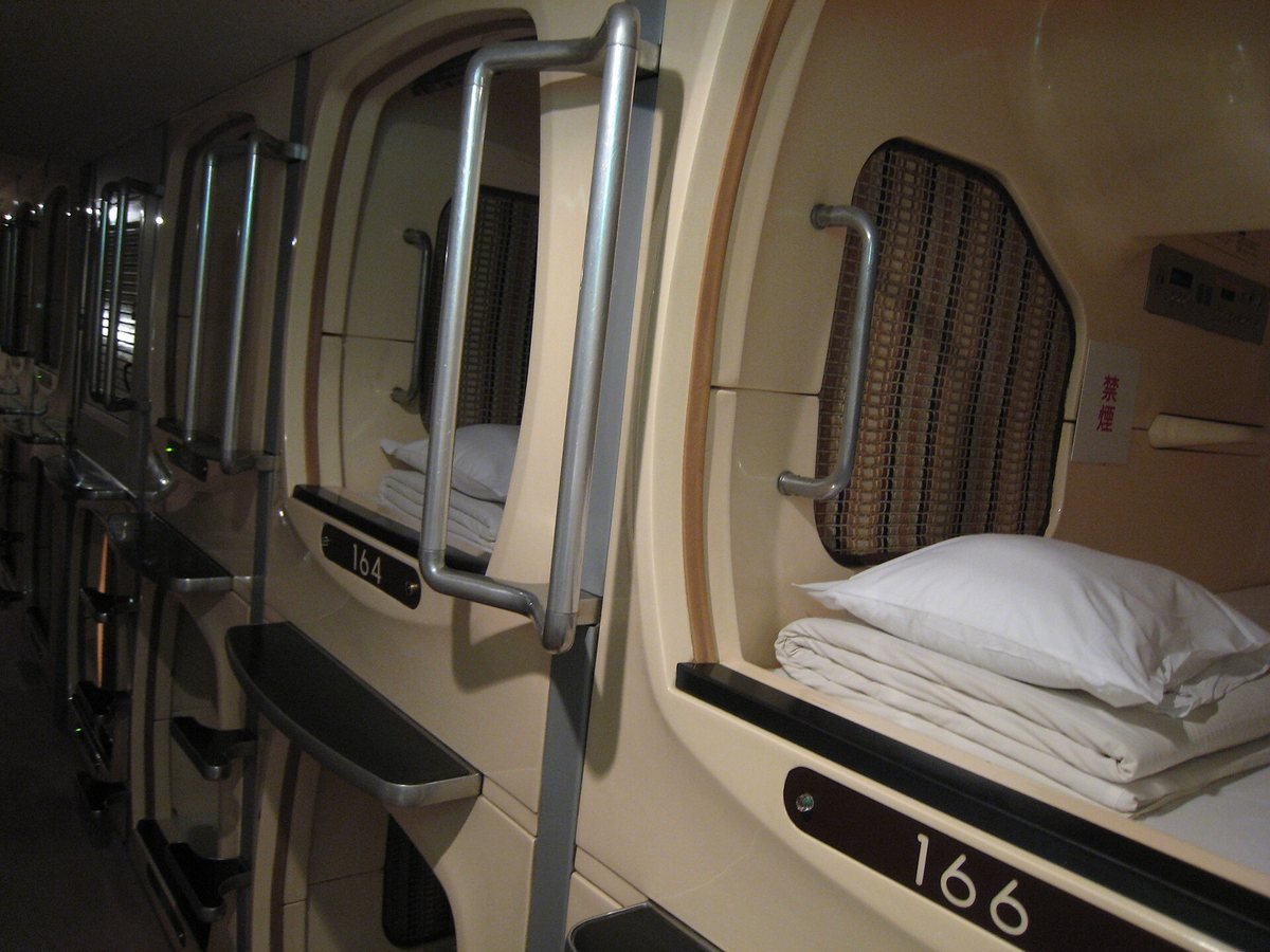 Two rows of stacked capsule pods with numbered entrances along a corridor in an Osaka capsule hotel