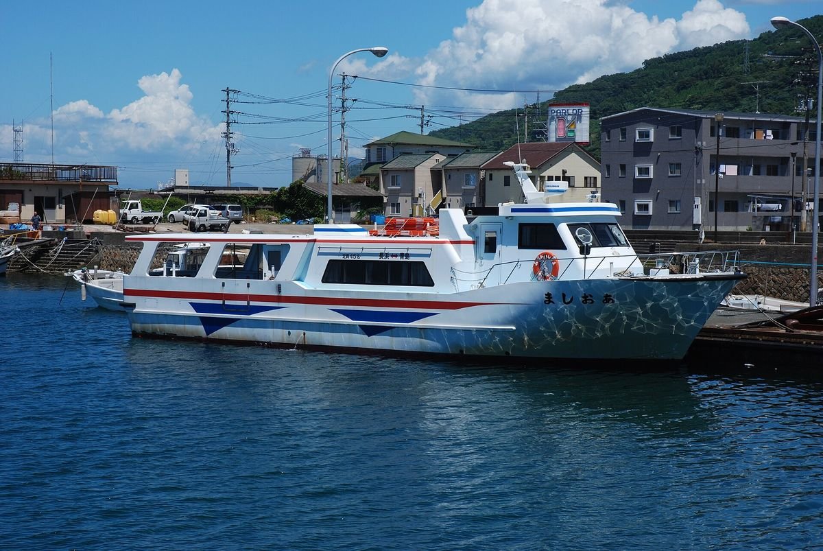 The small white passenger boat Aoshima moored in Nagahama harbor with hills and houses behind