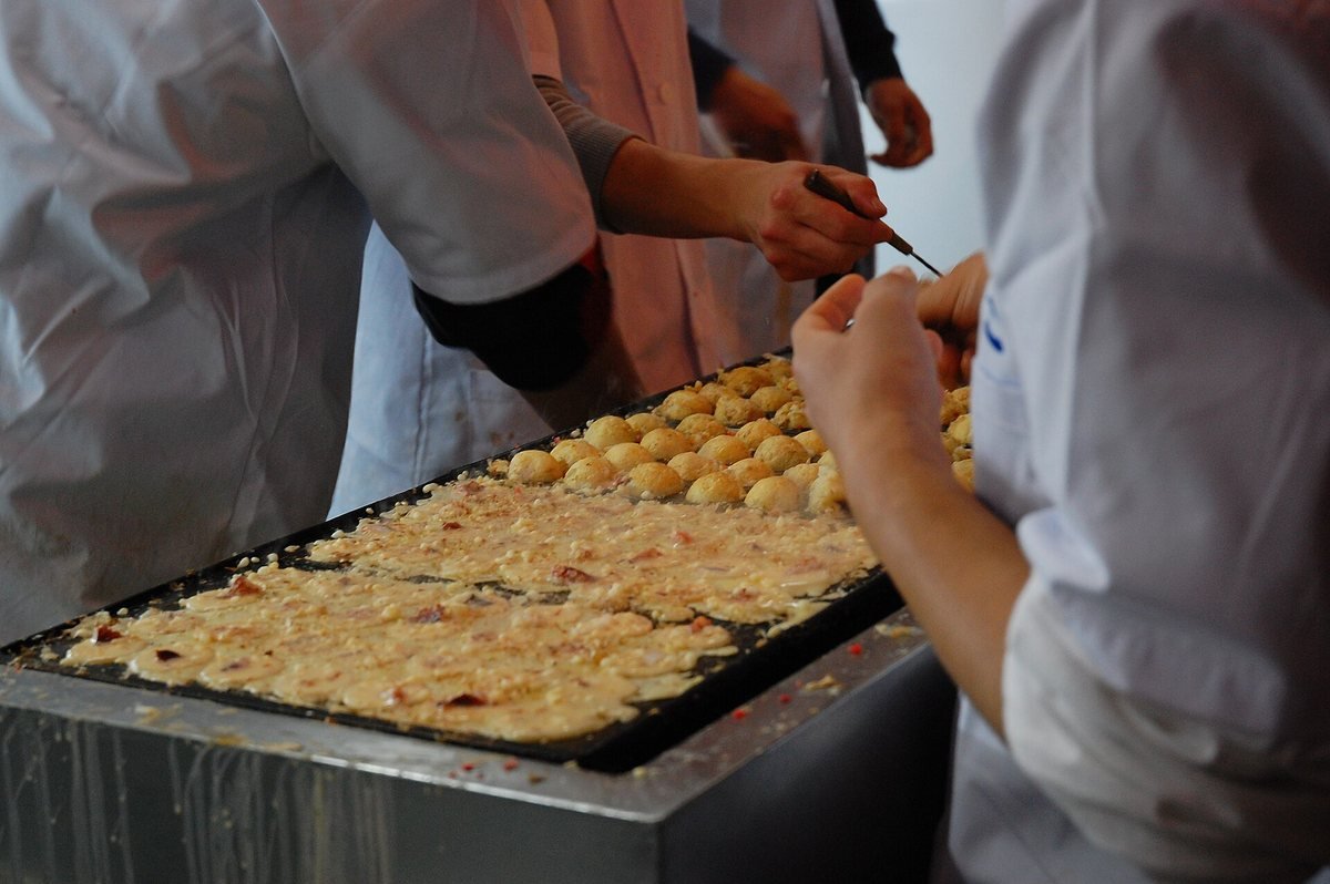 Cooks turning rows of takoyaki octopus balls on a large cast-iron griddle at a stand in Dotonbori, Osaka