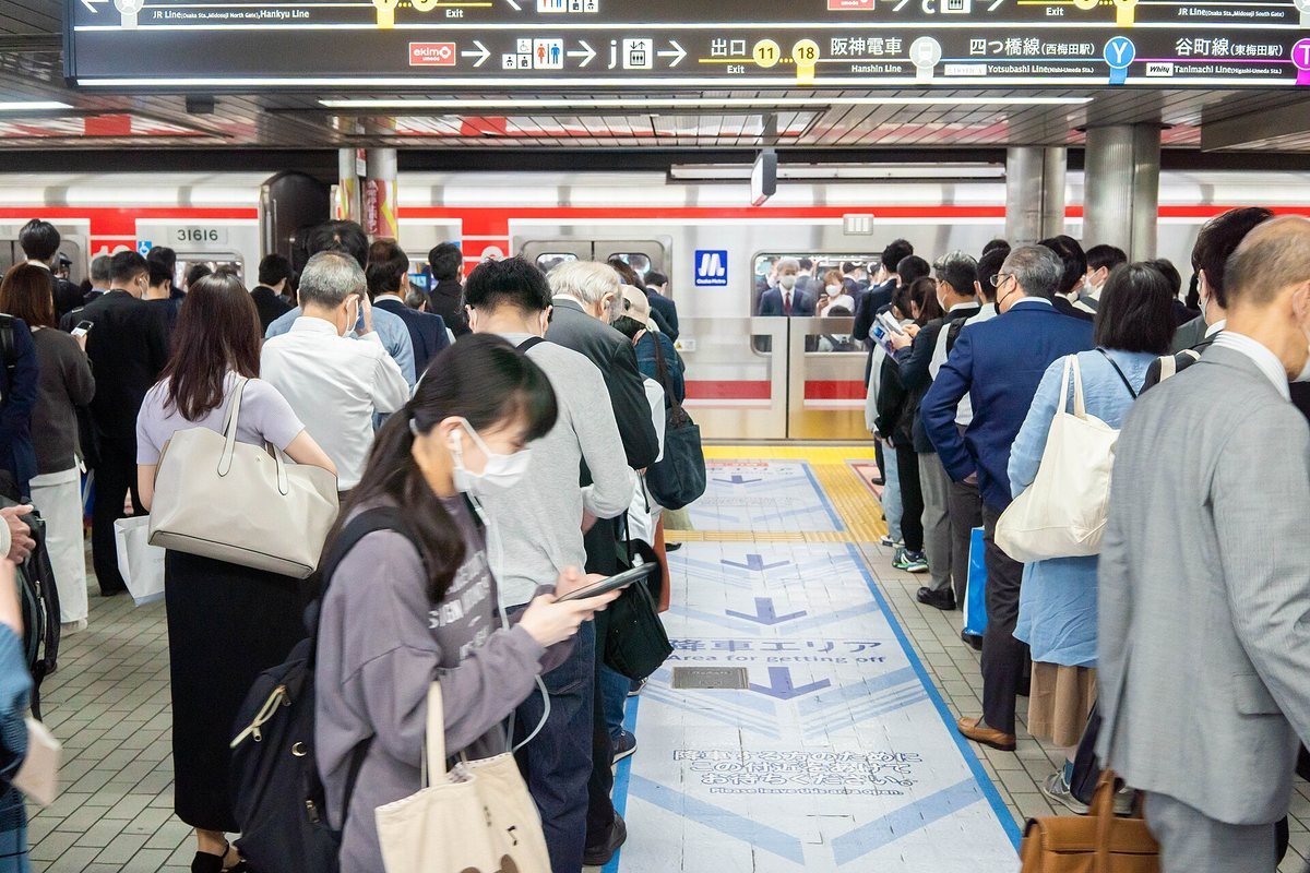 Commuters queueing in marked lines on an Osaka Metro platform at Umeda Station during the morning rush