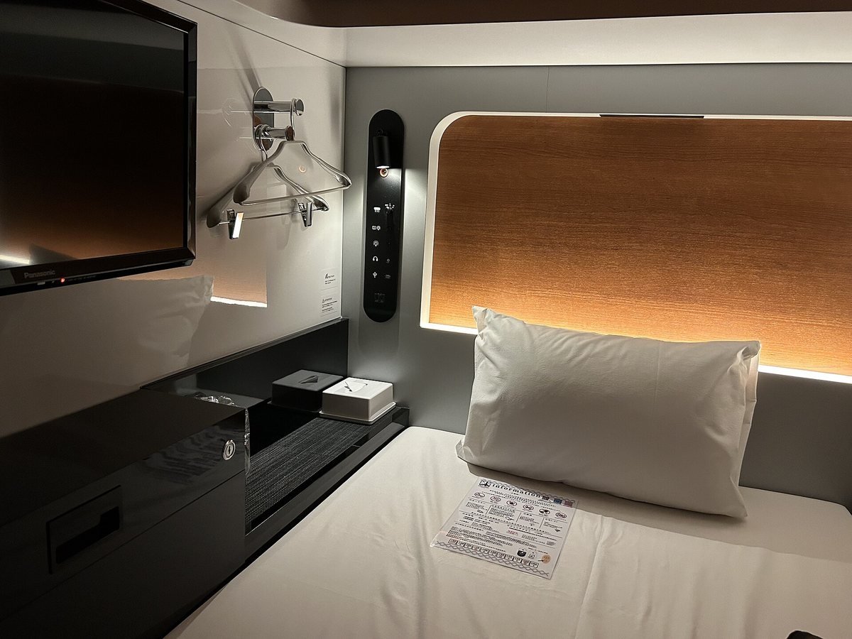 A First Cabin Premium Economy cabin in Ichigaya, Tokyo, with a made bed, wall-mounted TV and wood-panel headboard