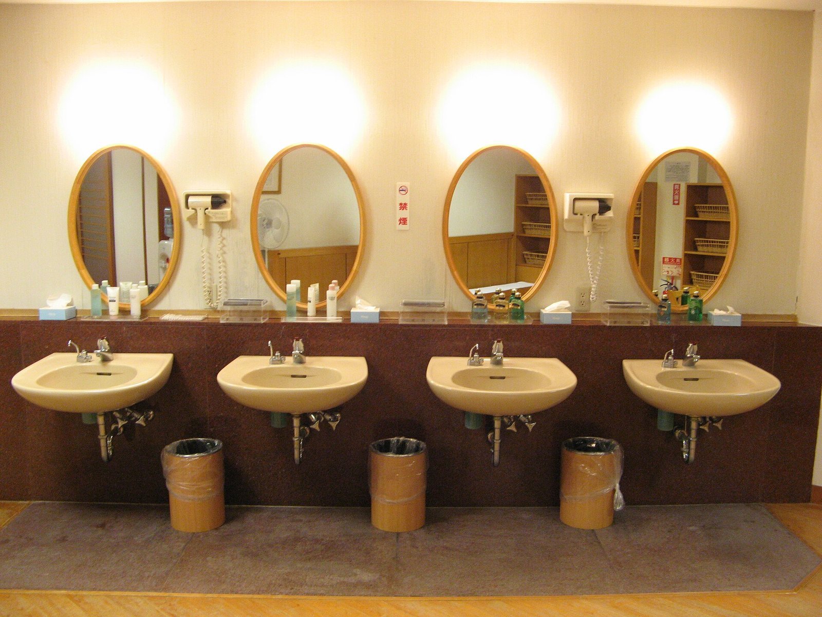Four oval mirrors, washbasins and hairdryers above a wooden counter in a Japanese onsen dressing room