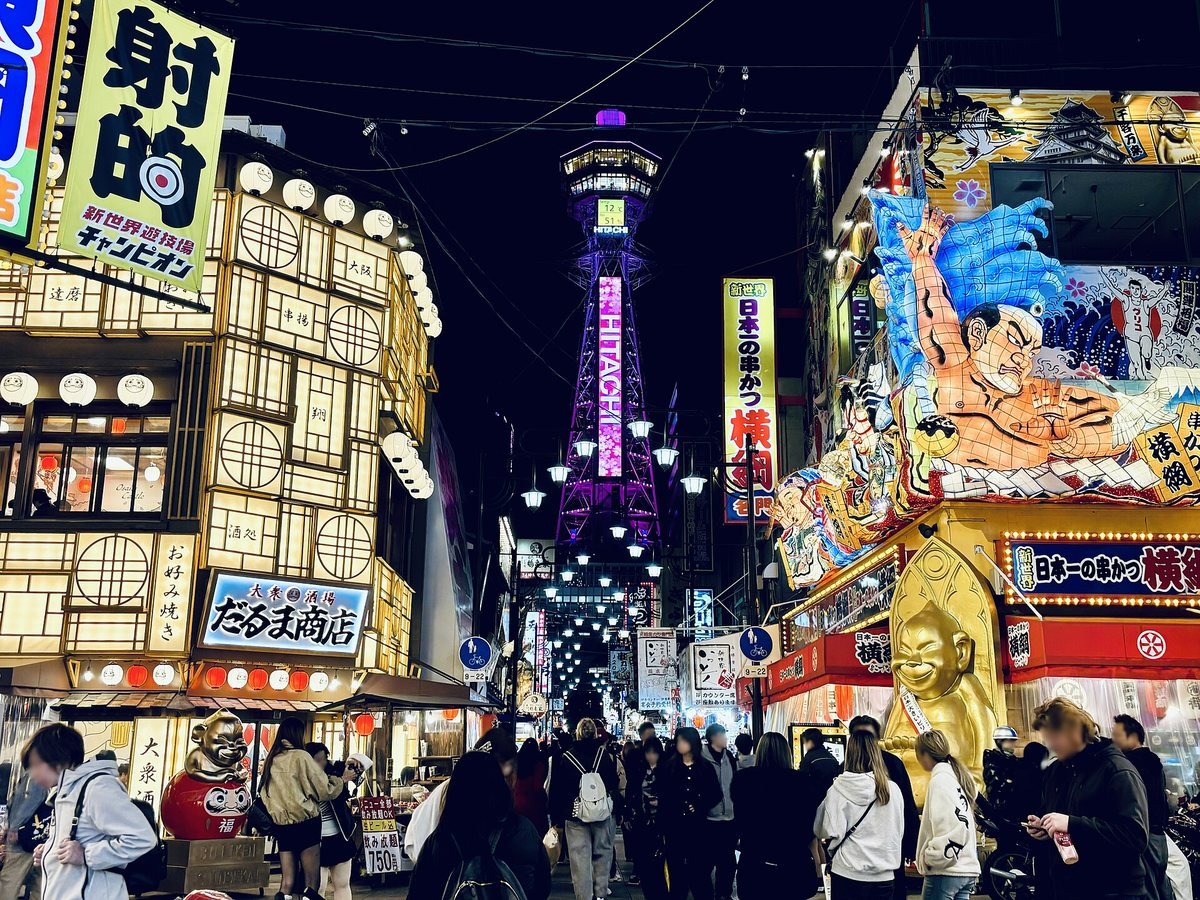 Shinsekai at night with bright shop signs, crowds on the street and the lit-up Tsutenkaku tower in the background