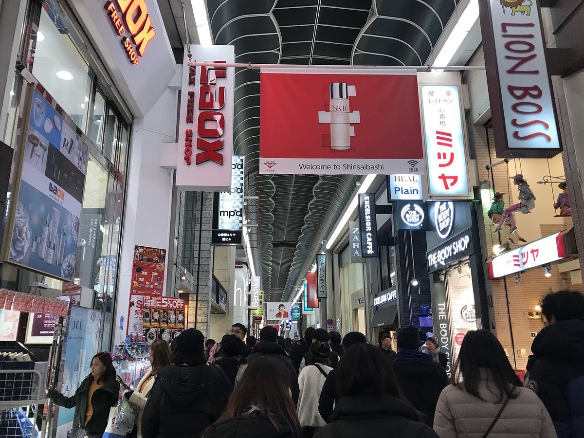 Shoppers walking under the covered arcade of Shinsaibashi-suji shopping street in Osaka with store signs overhead