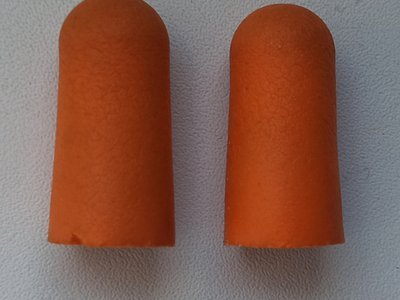 A pair of orange foam earplugs on a grey surface (item type photo, not the exact product)