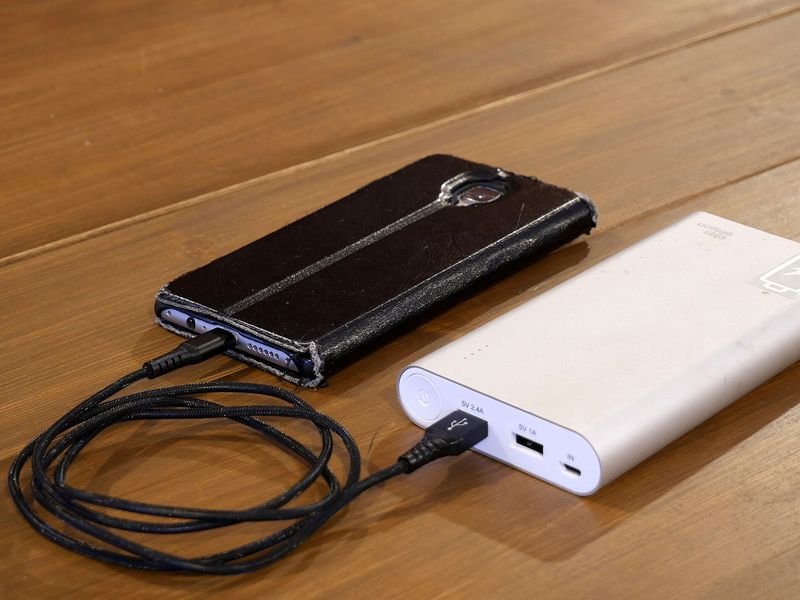 A white power bank charging a smartphone on a wooden table (item type photo, not the exact product)